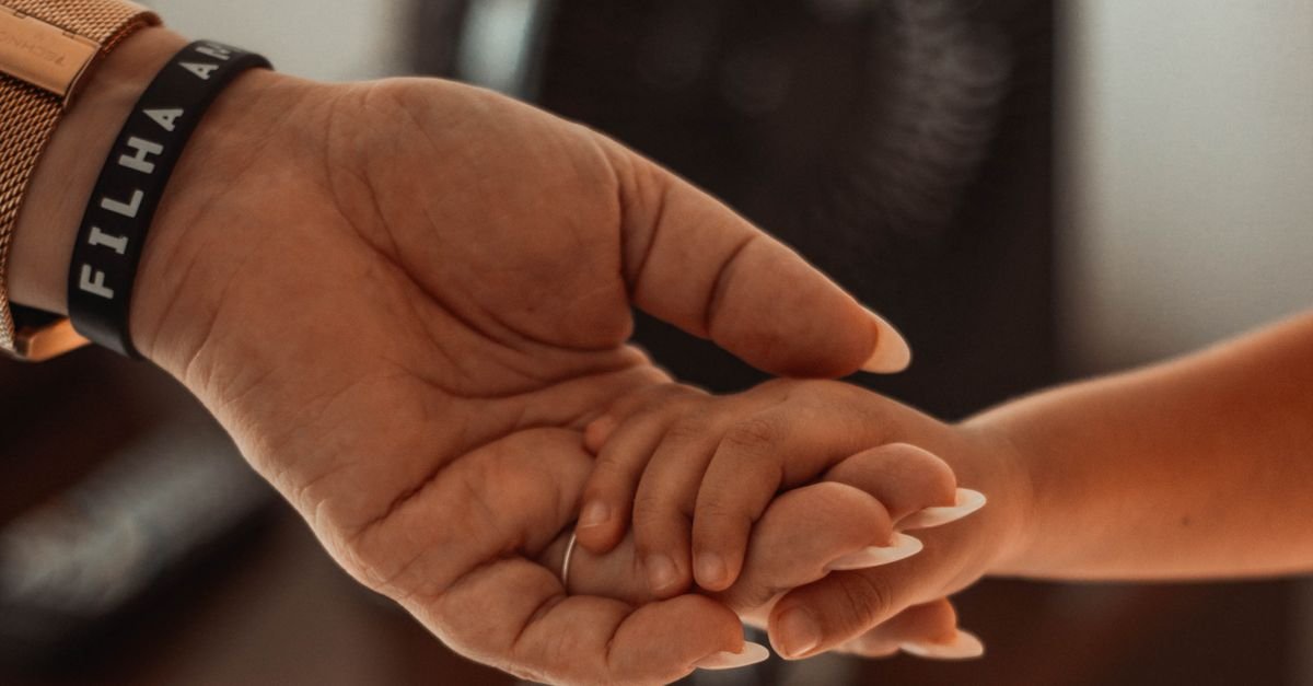 Mão de adulto segurando a mão de uma criança pequena em close