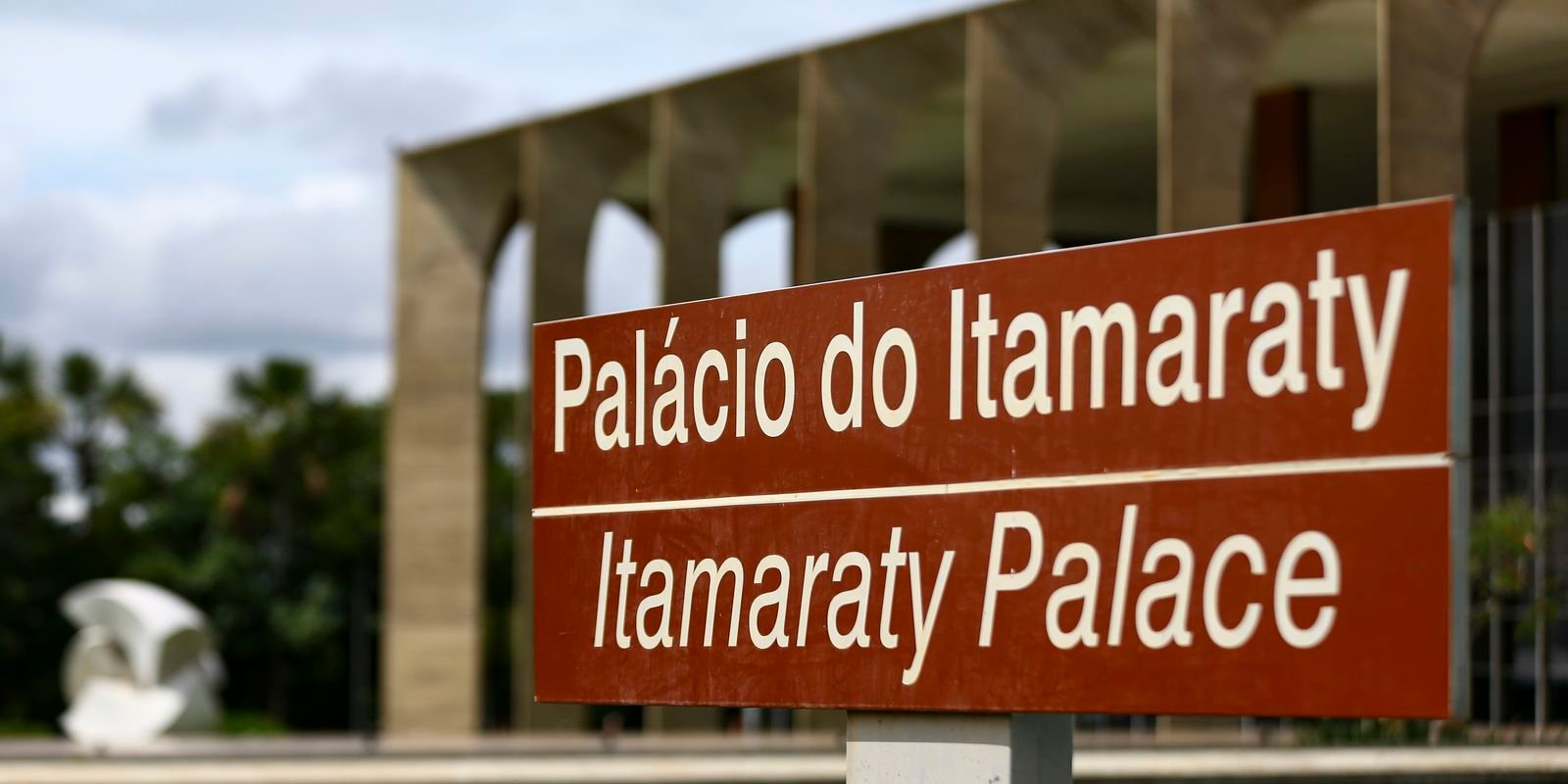 Placa bilíngue do Palácio do Itamaraty em Brasília, com os arcos da fachada ao fundo
