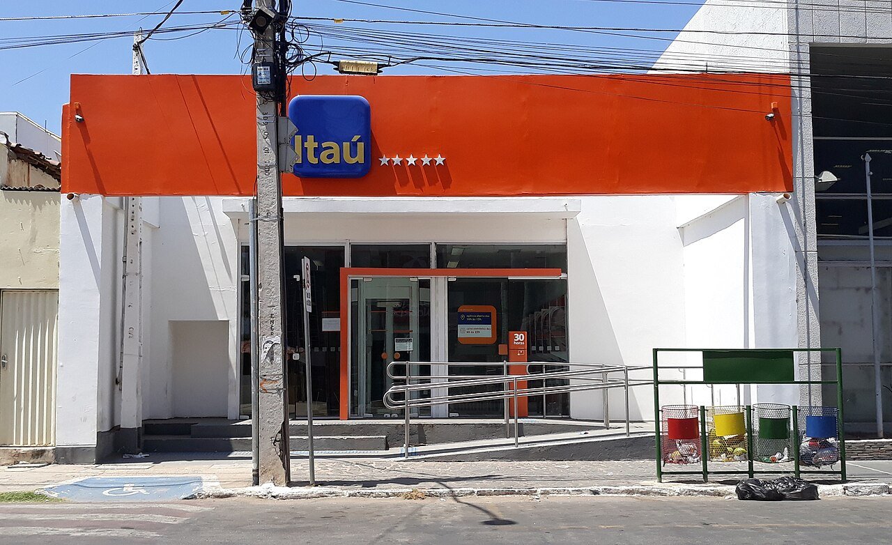 Fachada de agencia do banco Itau com letreiro laranja e azul em rua comercial