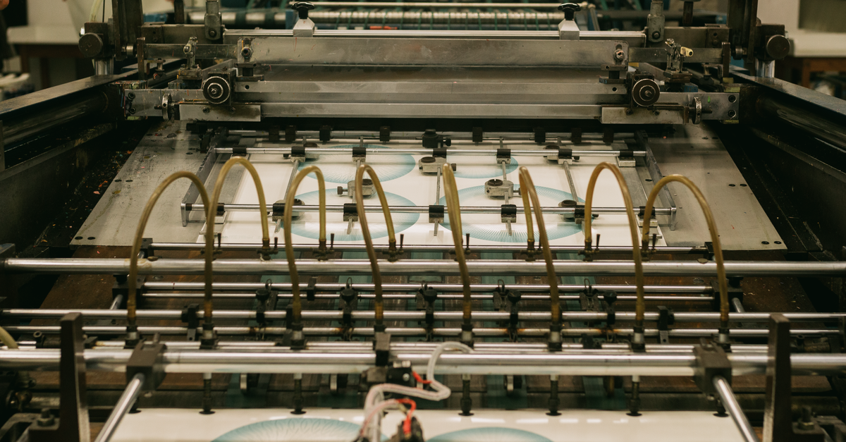 Detalhe de uma máquina de impressão industrial com rolos e folhas de papel