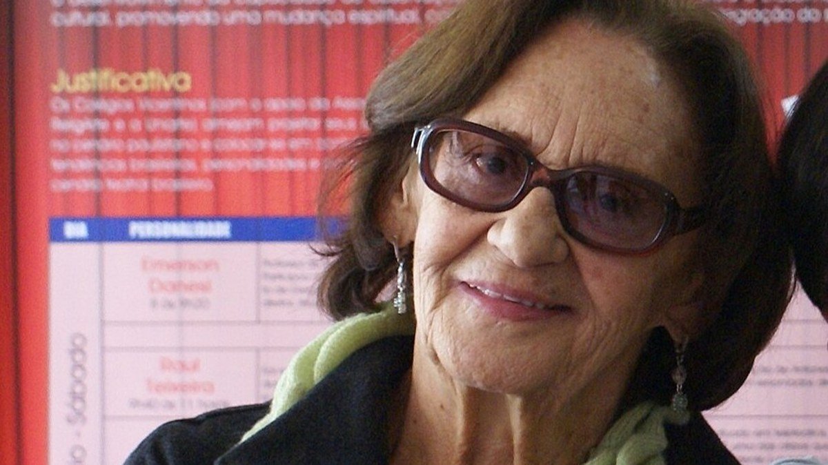 A atriz Laura Cardoso sorri diante de painel com o texto O Teatro como forma de Educação
