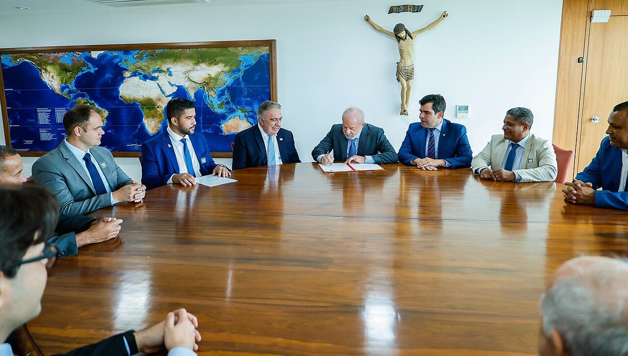 Presidente assina documento em mesa de reuniões do Palácio do Planalto, cercado por parlamentares