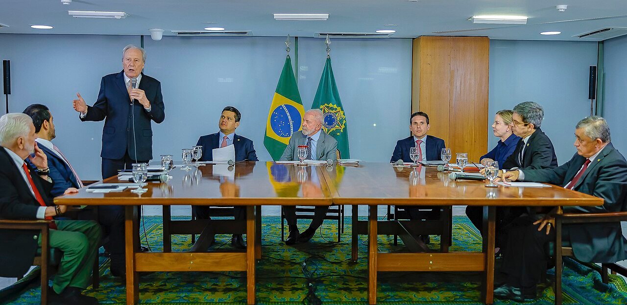 Reunião do presidente Lula com autoridades em torno de mesa de reuniões, com bandeiras do Brasil ao fundo