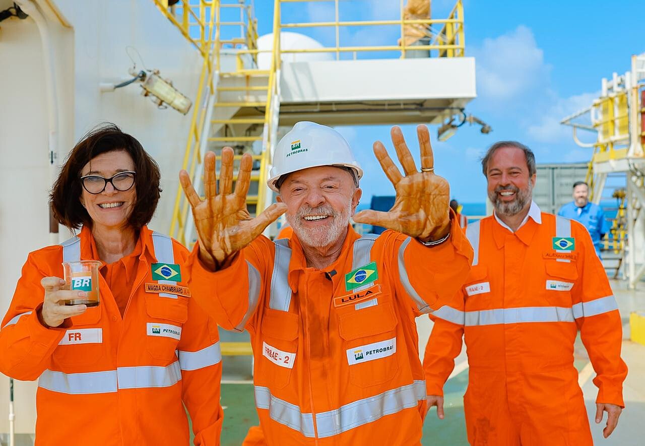 Lula de macacão da Petrobras mostra as mãos sujas de petróleo em navio-sonda, ao lado de Magda Chambriard e Alexandre Silveira