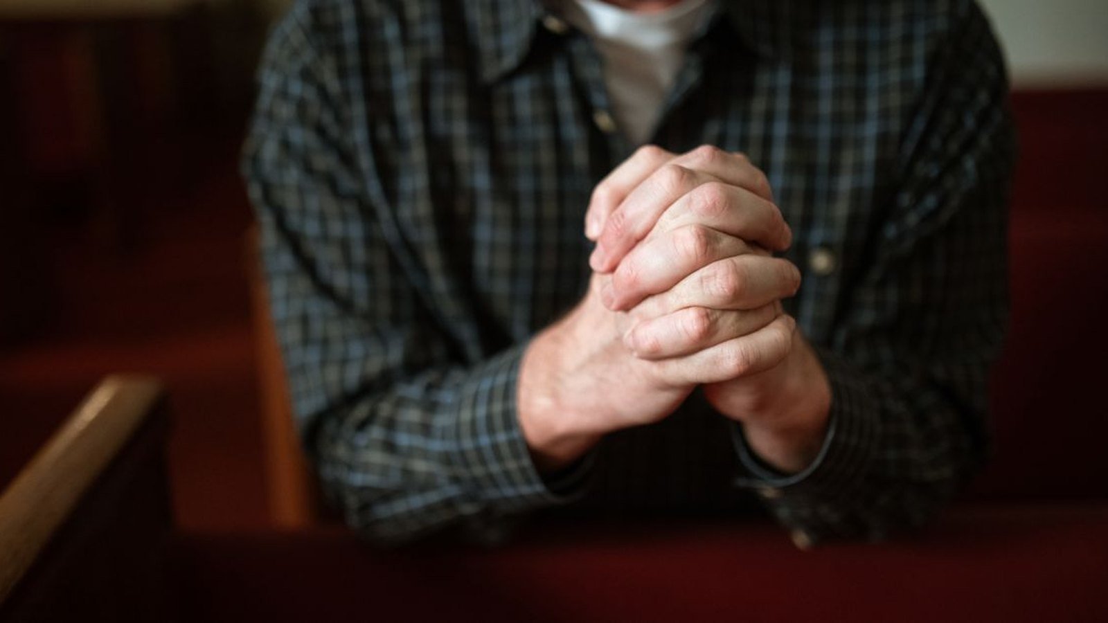 Fiéis com as mãos unidas em oração num banco de igreja