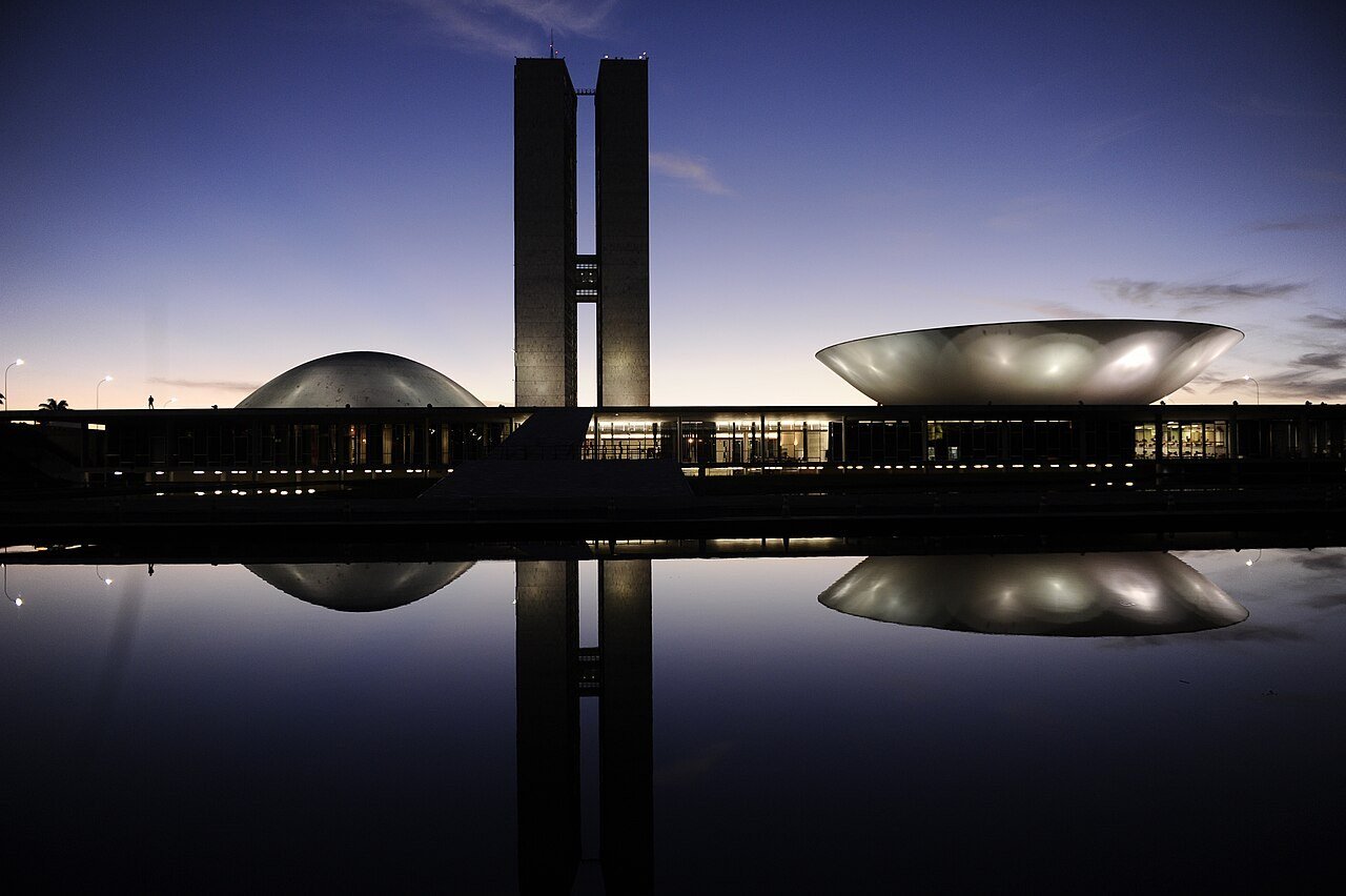 Edifício do Congresso Nacional em Brasília ao entardecer, com as duas torres e as cúpulas refletidas no espelho d'água