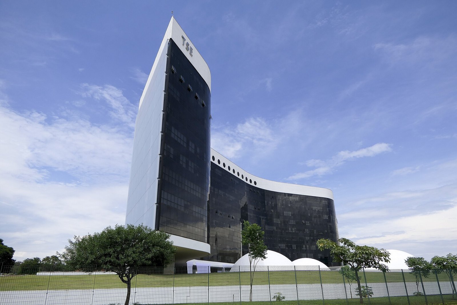 Sede do Tribunal Superior Eleitoral em Brasília, com a torre e o prédio curvo de vidro escuro sob céu azul