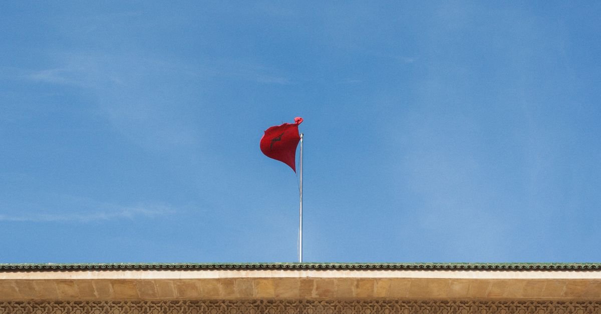Bandeira do Marrocos hasteada sobre edifício, com céu azul ao fundo