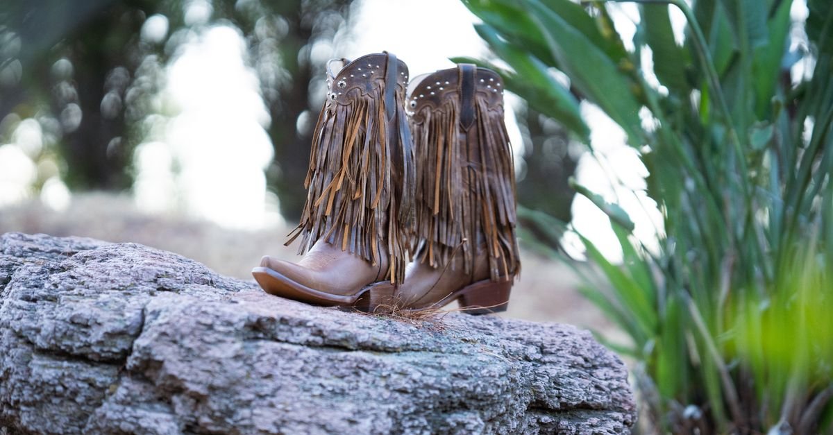 Par de botas de couro com franjas apoiado sobre uma pedra em area rural