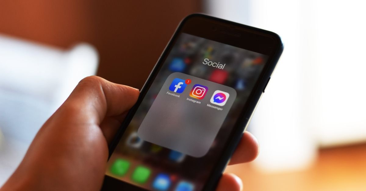 Mão segura um celular com ícones de redes sociais, entre eles Facebook, Instagram e Messenger