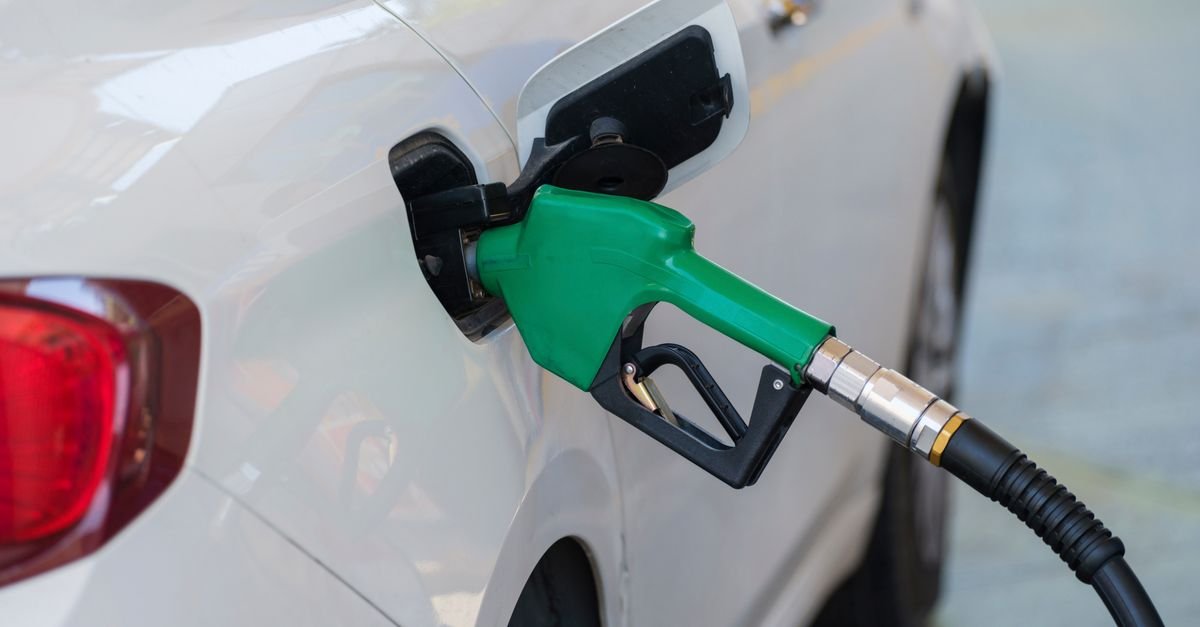 Bico de abastecimento verde inserido no tanque de um carro branco em posto de combustível