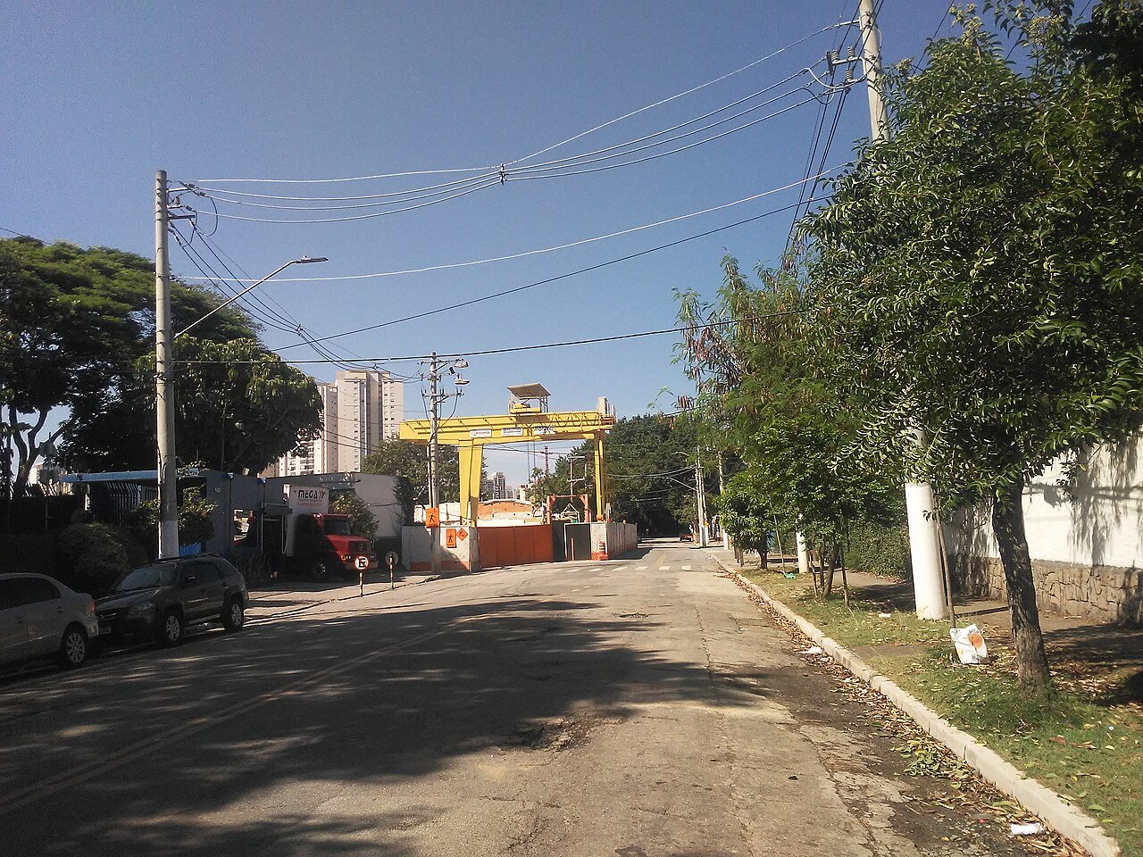 Canteiro de obras de estação de metrô com pórtico amarelo e tapumes em via urbana