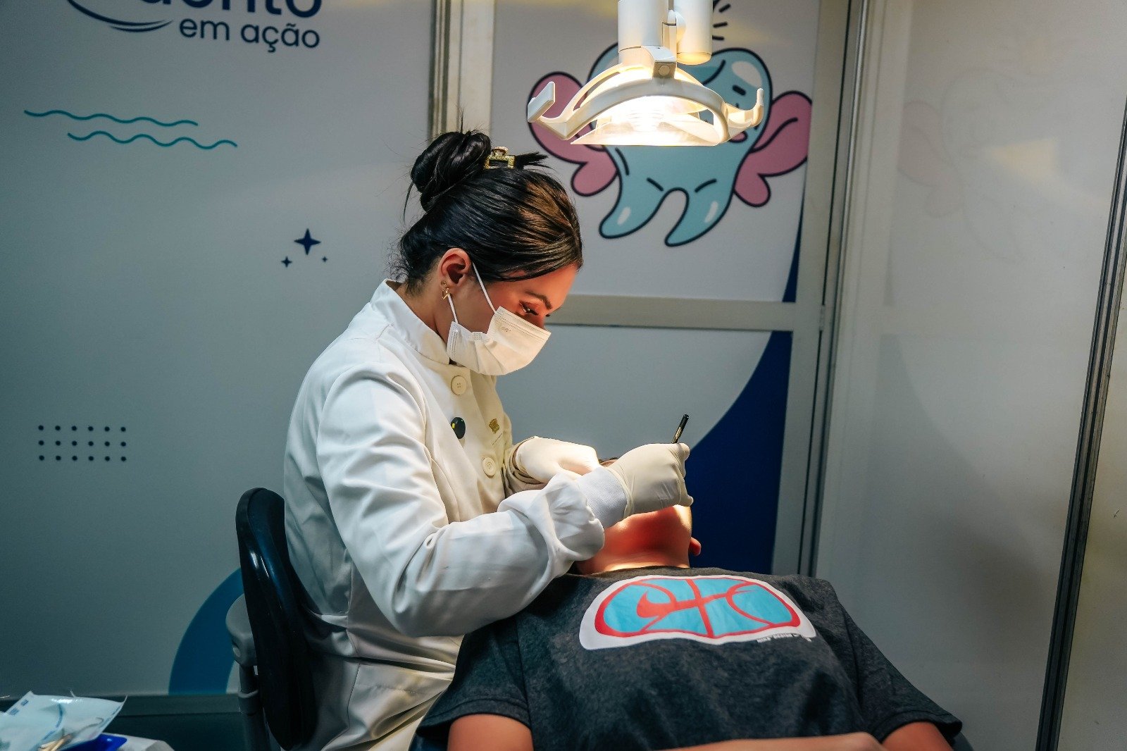 Dentista de jaleco branco e mascote em forma de dente na unidade do Odonto em Ação