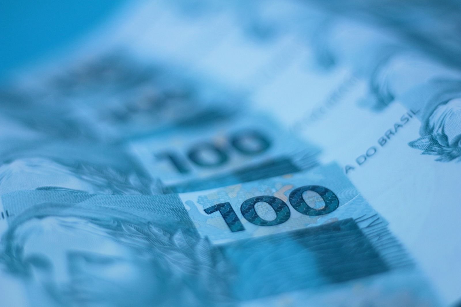 Notas de 100 reais em close, com foco na cédula do primeiro plano