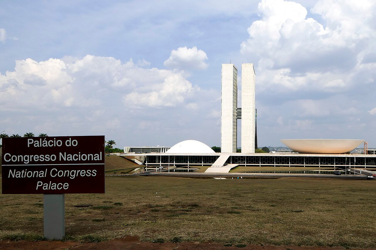Placa do Palácio do Congresso Nacional em primeiro plano, com as torres e as cúpulas do Congresso ao fundo