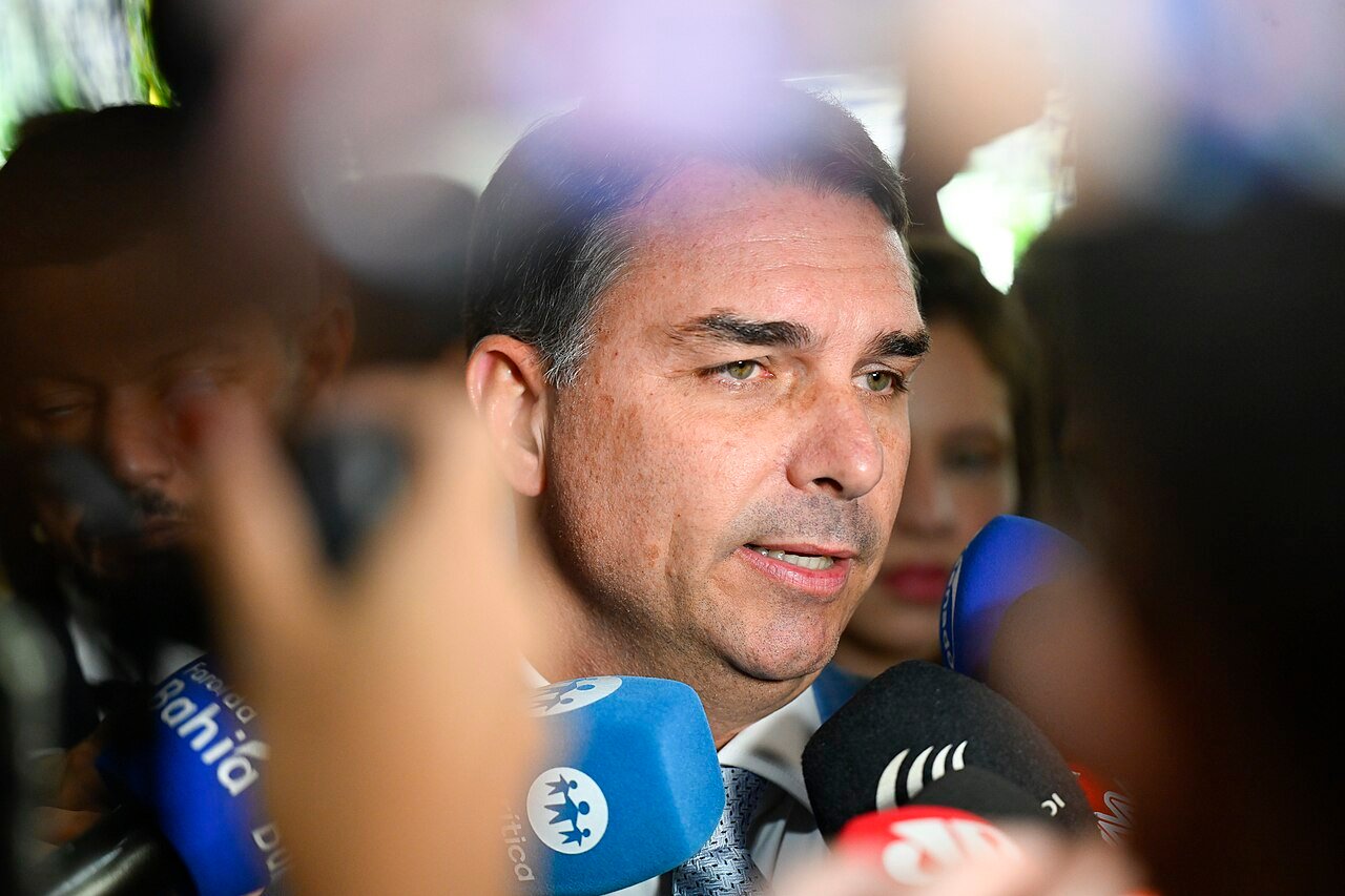 Senador Flavio Bolsonaro falando a jornalistas cercado por microfones durante entrevista
