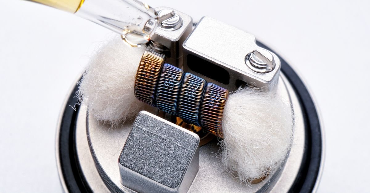 Close-up da resistência de um cigarro eletrônico sendo umedecida com líquido, sobre base metálica