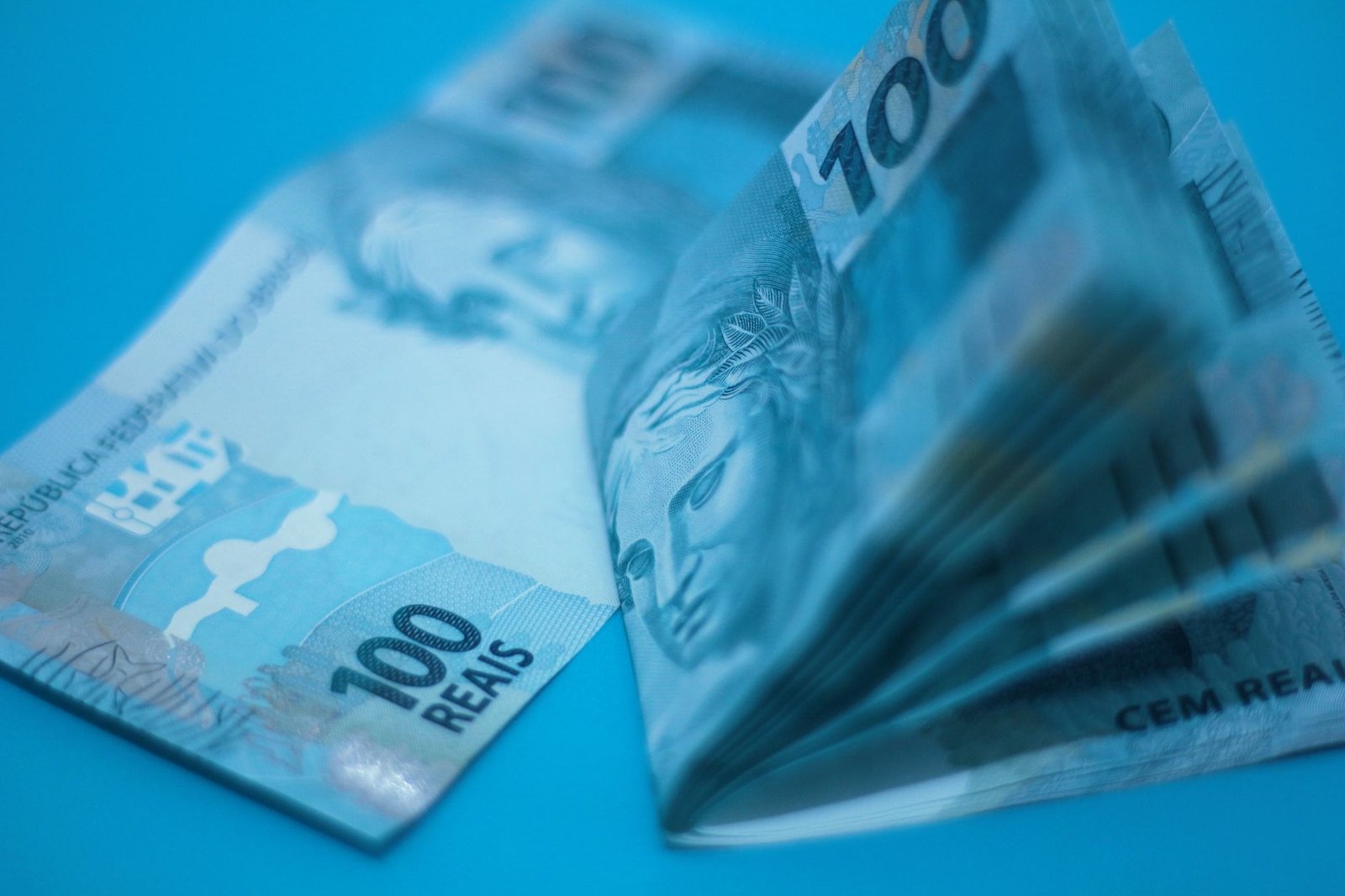 Cédulas de cem reais em close sobre fundo azul