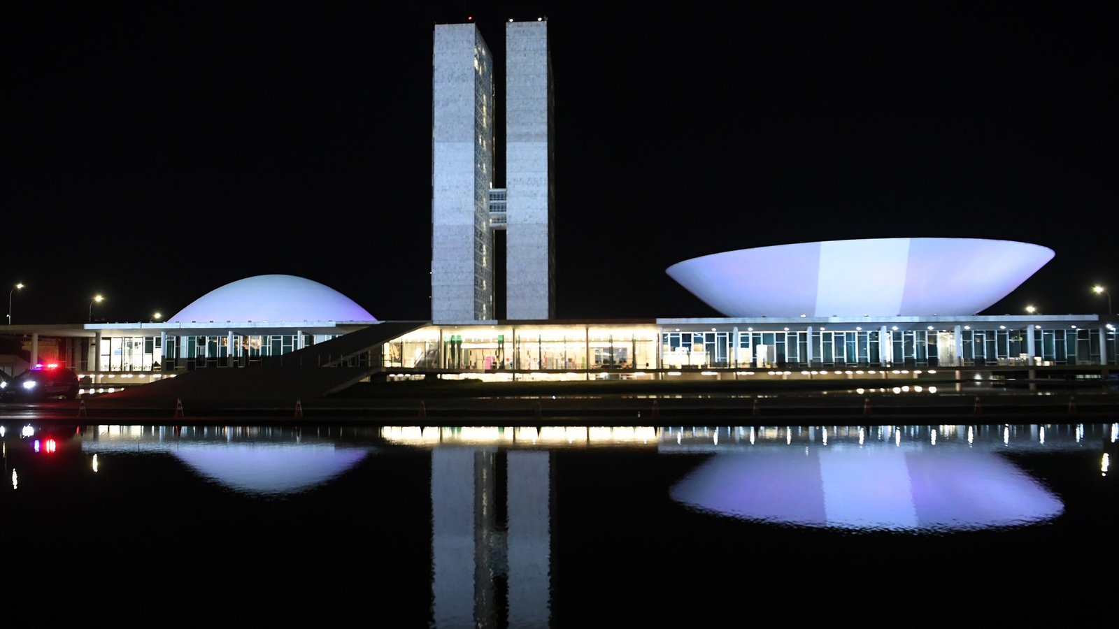 Palácio do Congresso Nacional iluminado à noite, com as cúpulas e as torres refletidas no espelho d'água