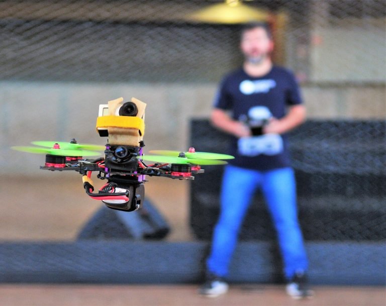 Drone em voo com operador ao fundo segurando o controle remoto