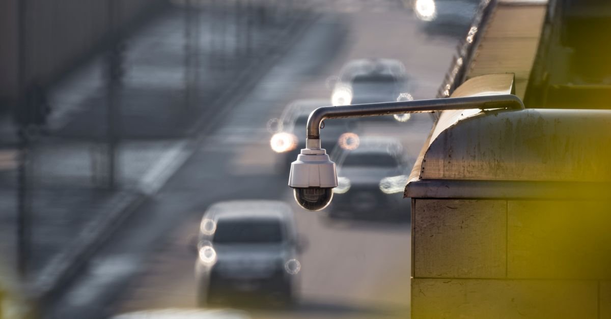 Câmera de videomonitoramento instalada sobre via urbana, com veículos desfocados ao fundo