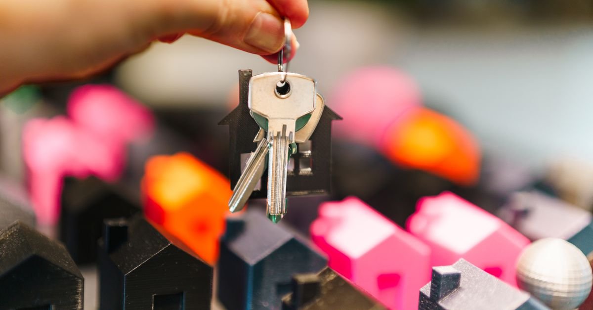 Mão segura um molho de chaves com chaveiro em formato de casa sobre miniaturas de casas