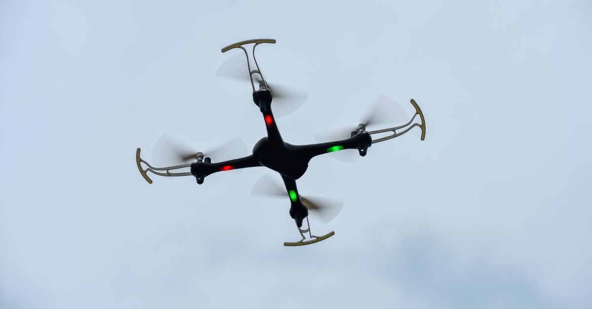 Drone quadricóptero preto em voo contra céu claro