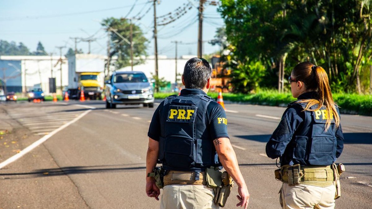 Dois policiais rodoviários federais de costas observando o trânsito em rodovia