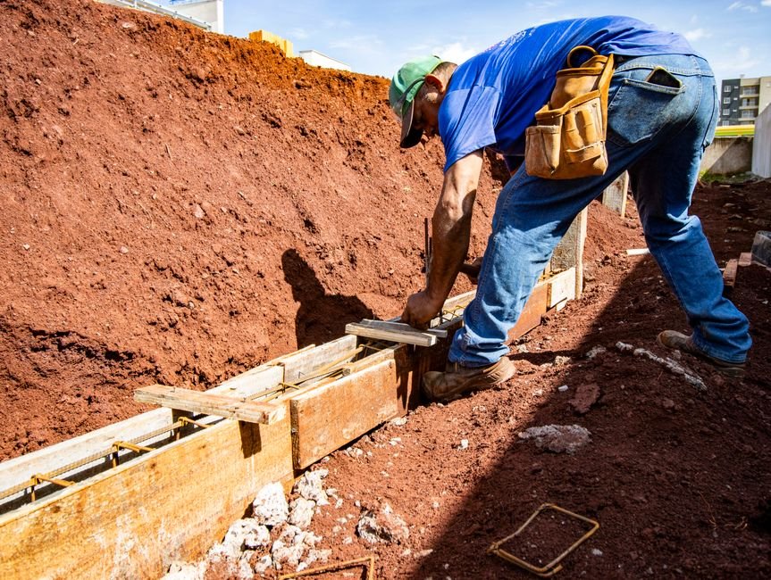Trabalhador da construcao civil montando forma de fundacao em canteiro de obras de terra vermelha