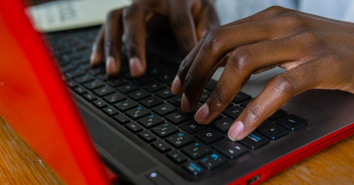 Mãos digitando no teclado de um notebook sobre mesa de madeira