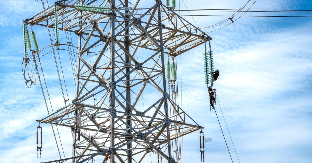 Trabalhador em torre de transmissão de energia elétrica sob céu azul
