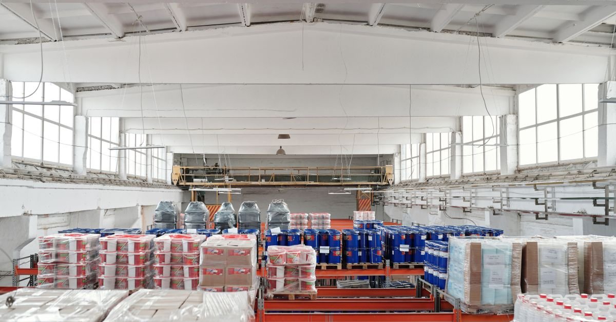 Interior de galpão de armazenagem com mercadorias paletizadas e envolvidas em filme plástico sobre estruturas porta-paletes