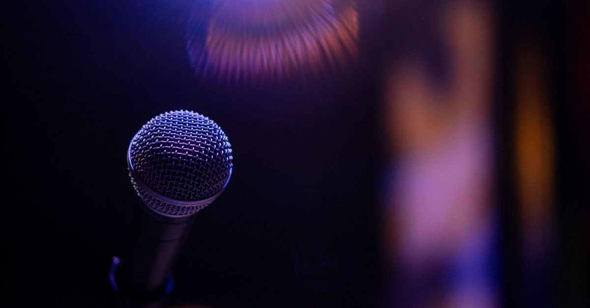 Microfone em close sob luz de palco, em imagem ilustrativa de debate