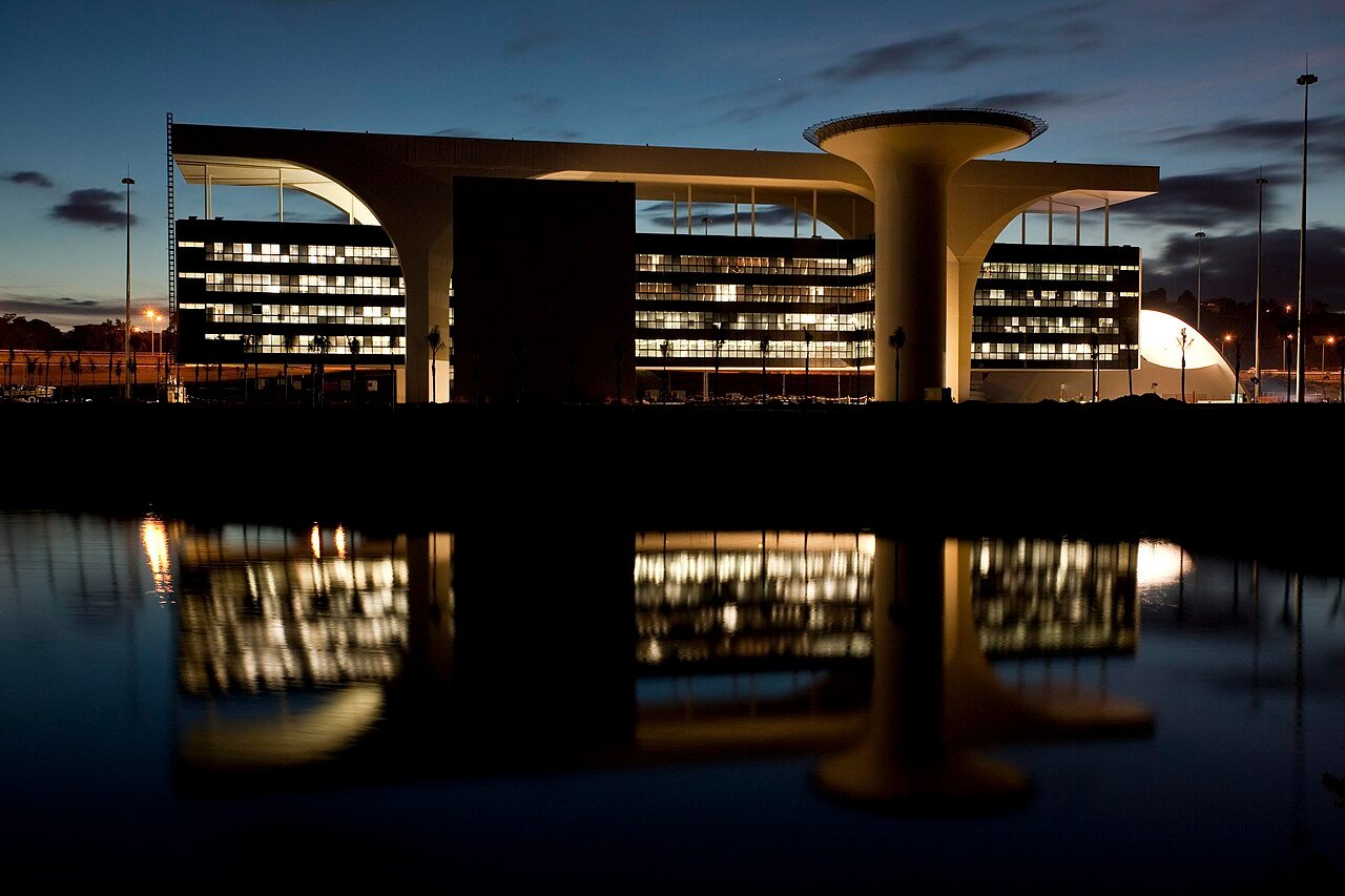 Prédio da Cidade Administrativa de Minas Gerais iluminado ao anoitecer, com reflexo no espelho d'água