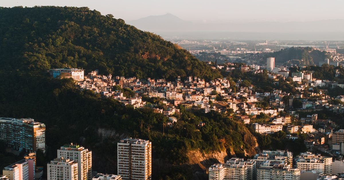 Vista aérea do Rio de Janeiro ao amanhecer, com morro e prédios residenciais