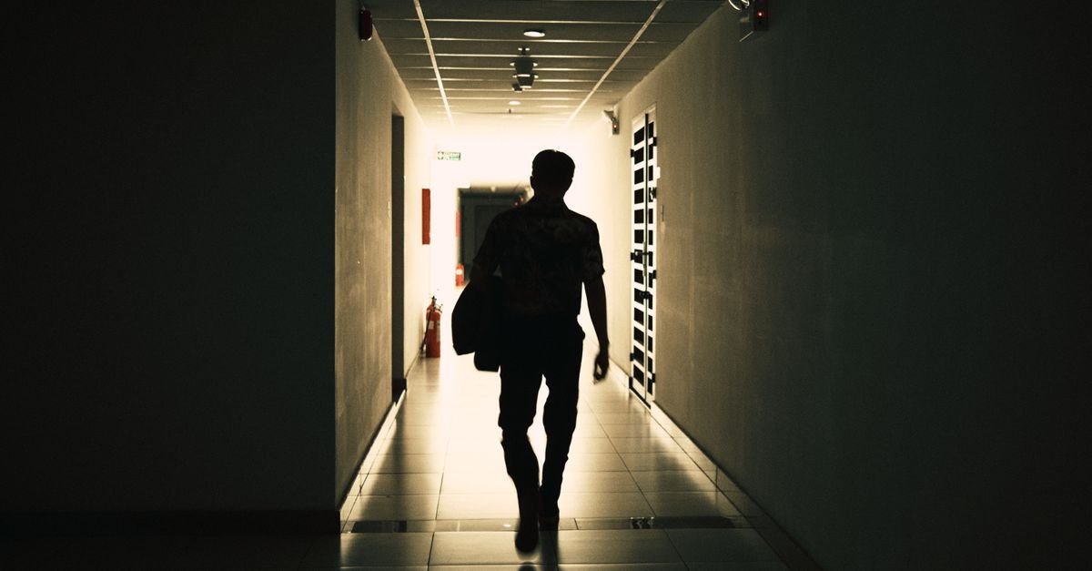 Silhueta de uma pessoa caminhando por corredor escuro em direção à luz