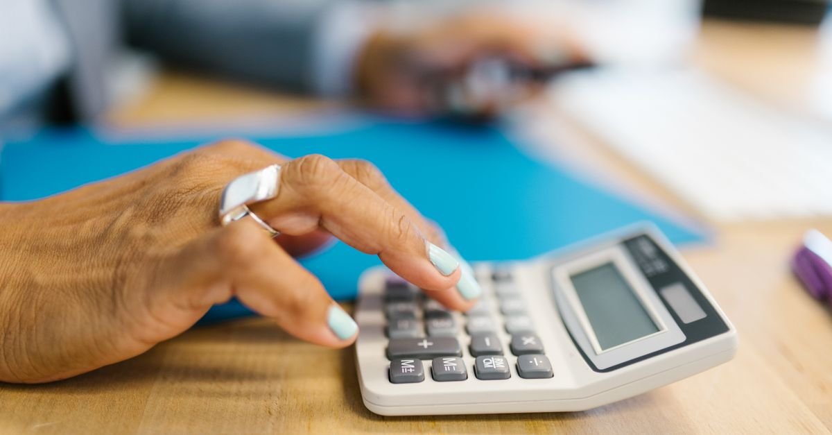 Mão de uma pessoa operando uma calculadora sobre uma mesa de madeira
