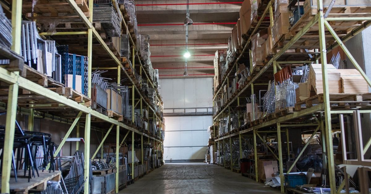 Corredor de galpão com prateleiras industriais carregadas de caixas e peças