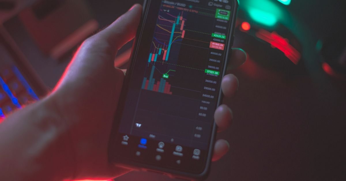 Mao segurando celular com aplicativo de negociacao de criptoativos na tela