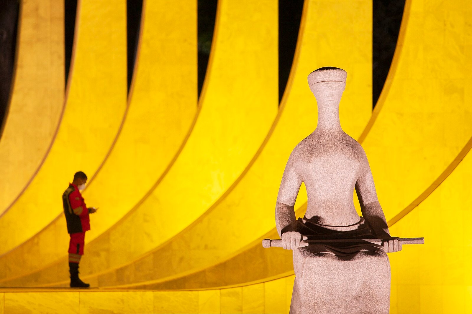 Escultura A Justica em primeiro plano diante da fachada iluminada do Supremo Tribunal Federal