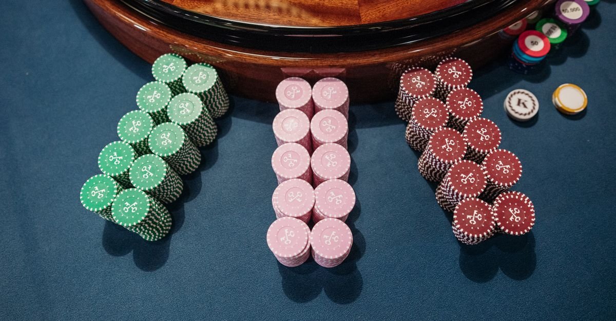 Fichas de cassino empilhadas sobre mesa de feltro azul ao lado da borda de uma roleta