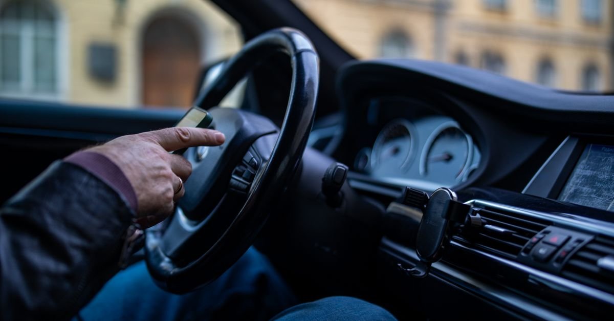 Mão de motorista no volante de um carro com suporte de celular no painel