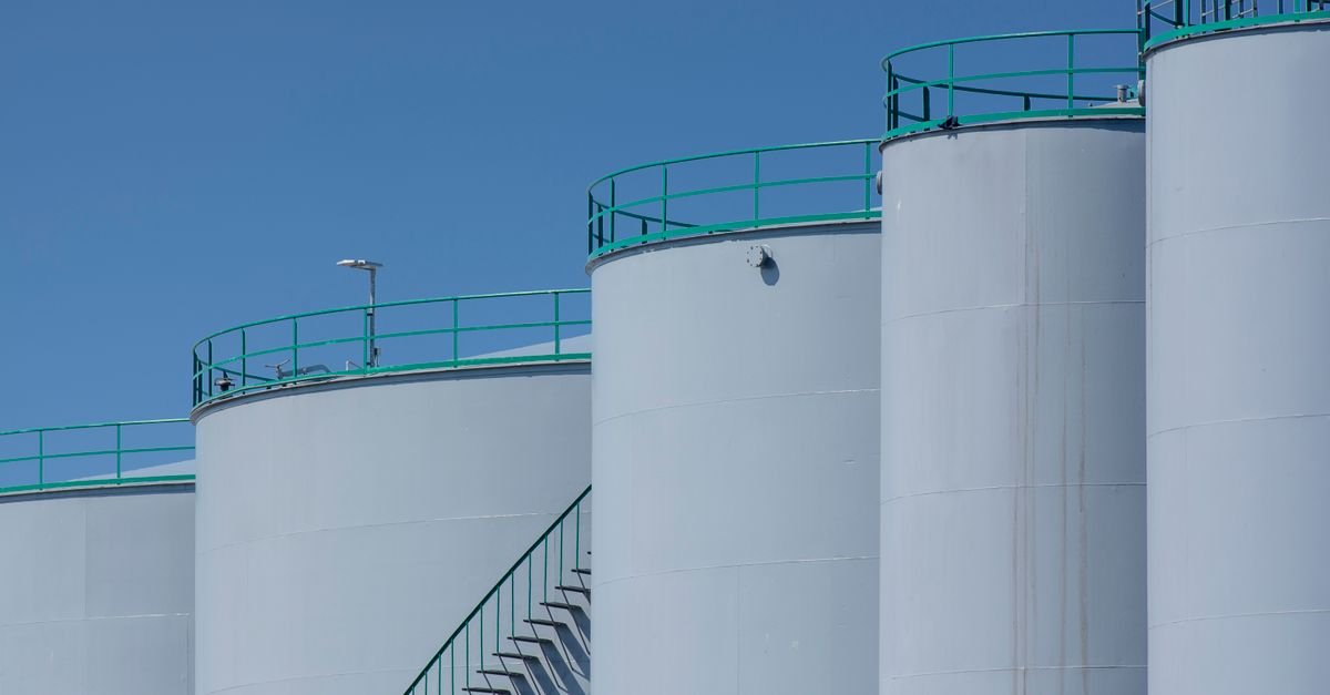 Fileira de tanques industriais brancos de armazenamento de combustível com passarelas metálicas, sob céu azul