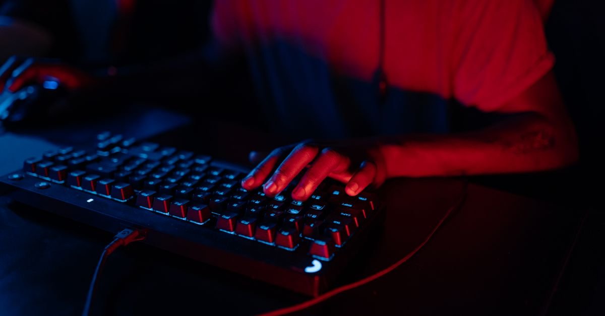 Mãos digitando em teclado retroiluminado em ambiente escuro com luz vermelha