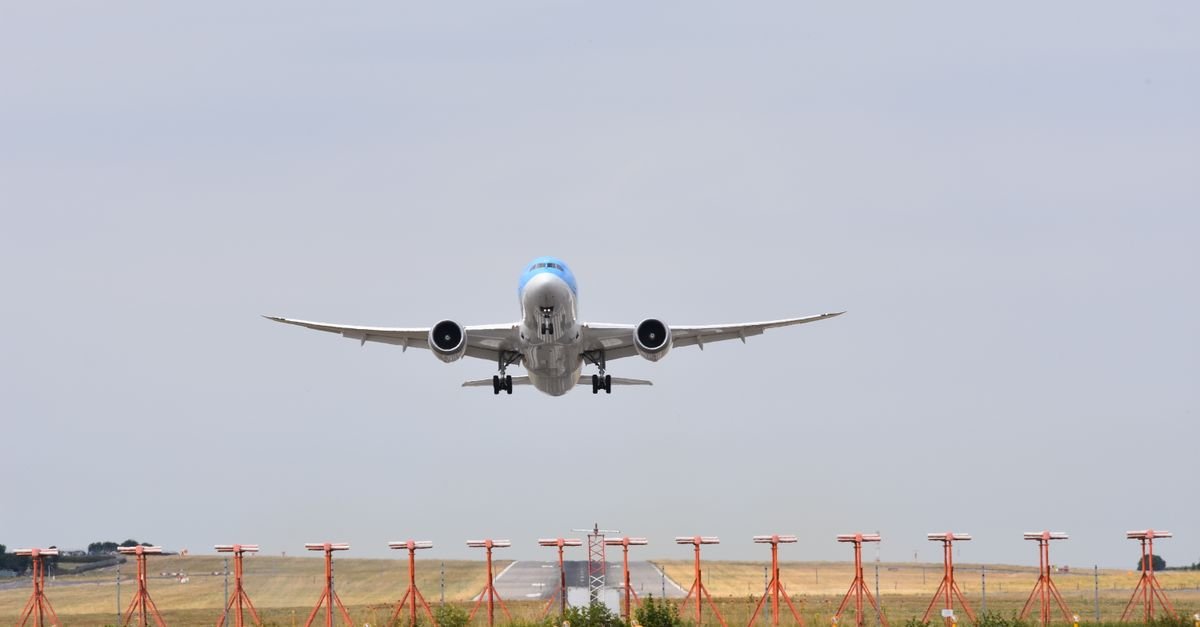 Avião de fuselagem larga decola de pista de aeroporto com balizadores em primeiro plano