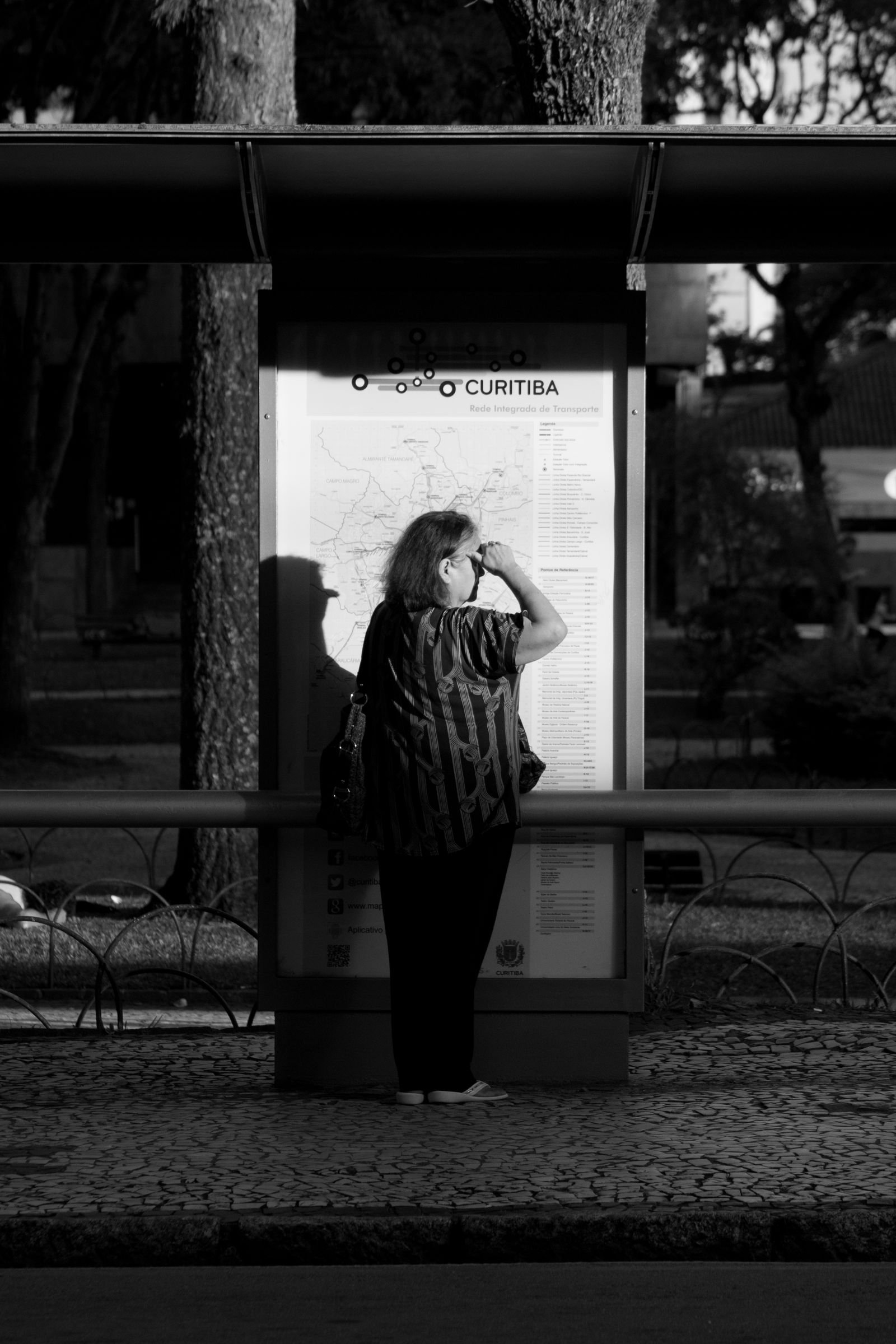 Mulher de costas observa mapa de transporte público em ponto de ônibus