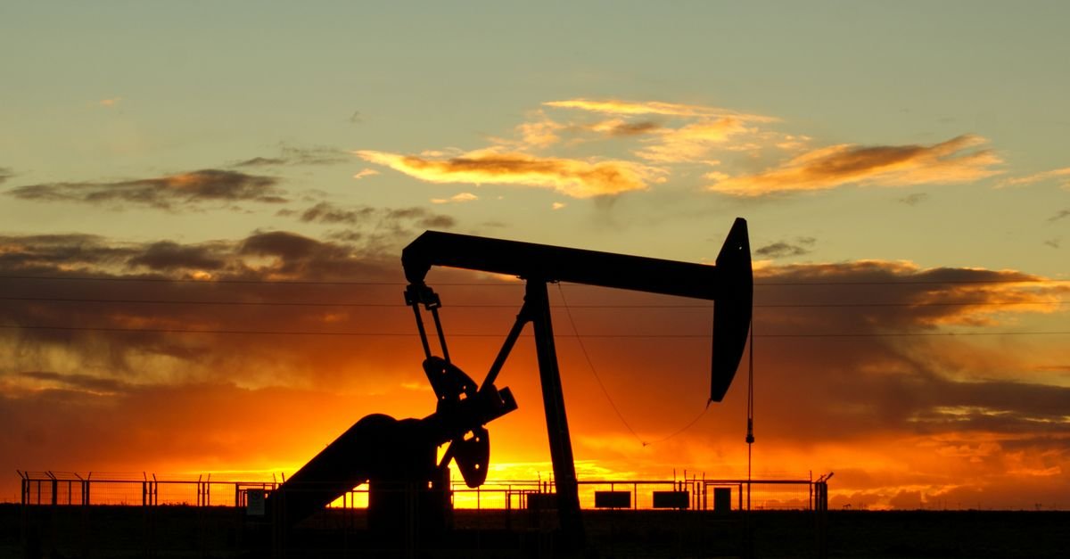 Silhueta de uma unidade de bombeio de petróleo contra o céu alaranjado no fim da tarde