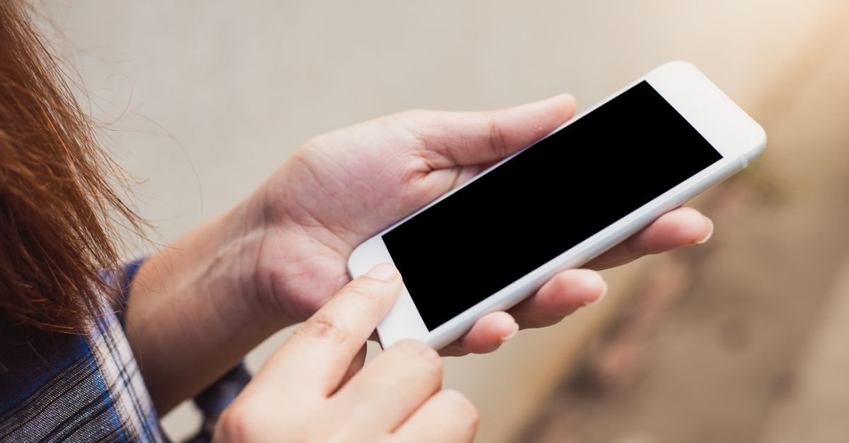 Pessoa segura smartphone com as duas mãos ao ar livre
