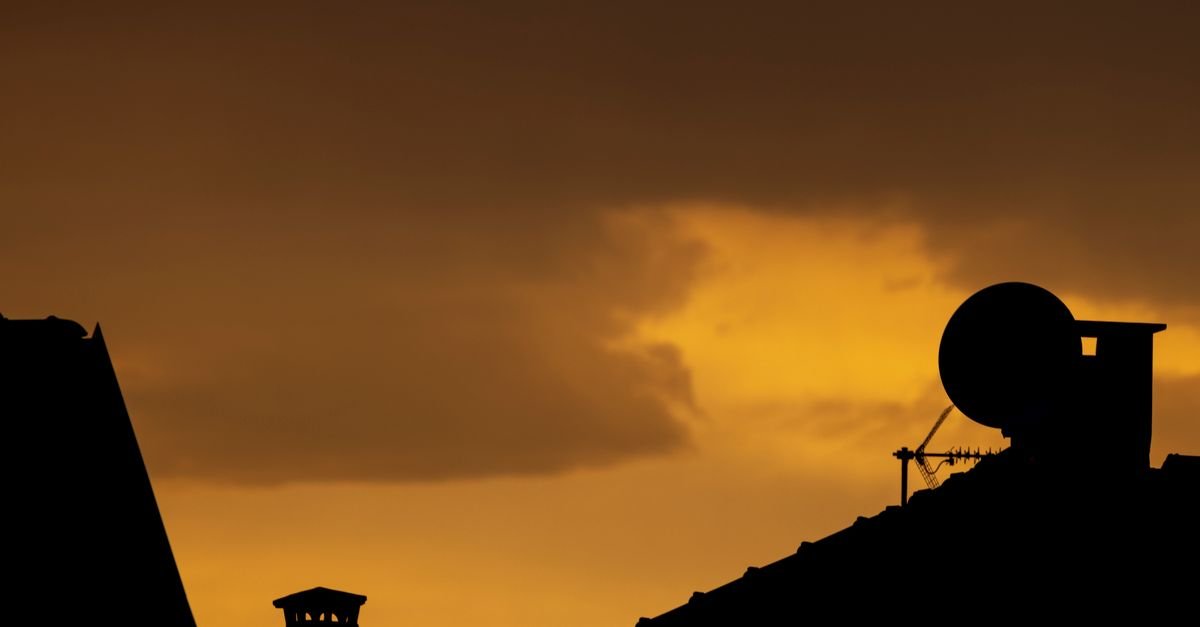 Silhueta de telhados com antena de televisão e antena parabólica contra o céu ao entardecer
