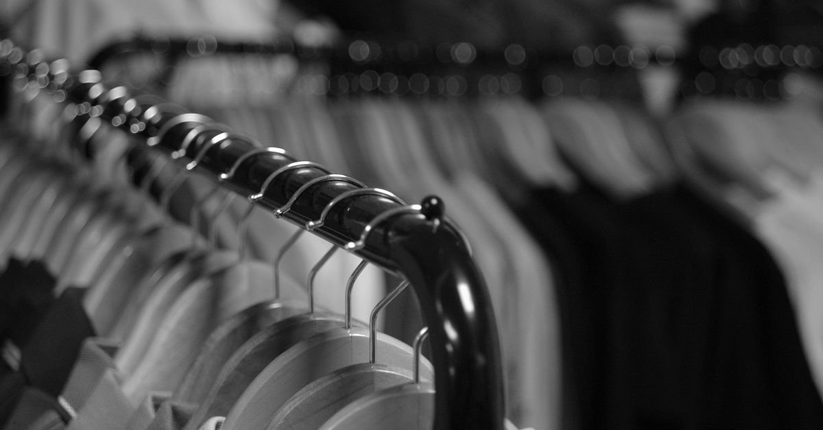 Araras de roupas com cabides em loja, em imagem preto e branco